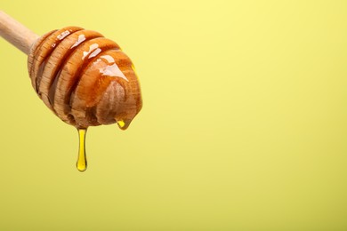 Photo of Delicious honey flowing down from dipper against yellow background, closeup. Space for text