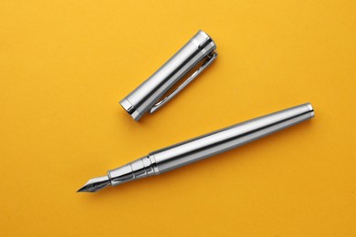 Photo of Stylish silver fountain pen with cap on yellow background, top view