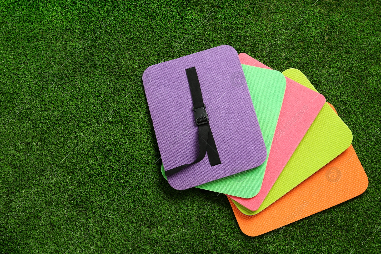 Photo of Bright foam tourist seat mats on green grass, flat lay. Space for text