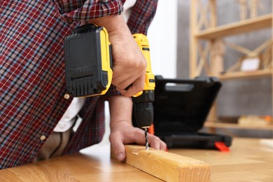 Photo of Young handyman working with electric drill at table in workshop, closeup