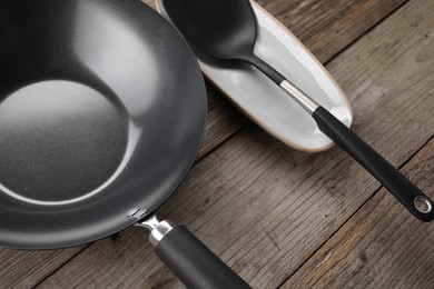 Black metal wok and spatula on wooden table, above view