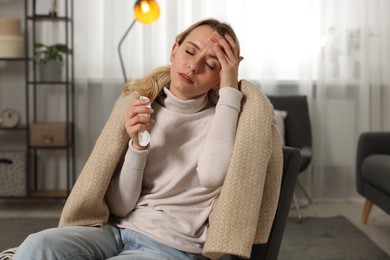 Sick woman wrapped in blanket with tissue in armchair at home. Cold symptoms