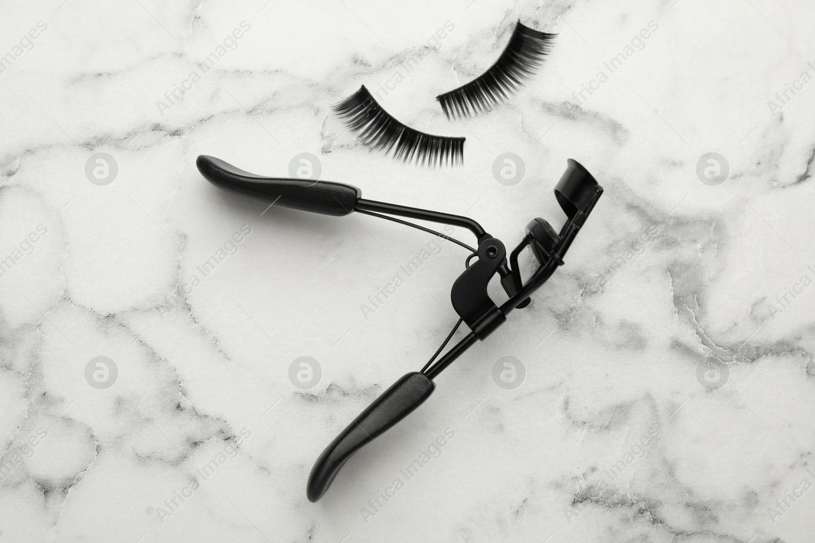 Photo of False eyelashes and curler on white marble table, flat lay