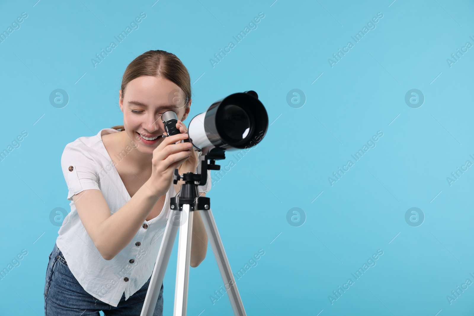 Photo of Happy astronomer looking at stars through telescope on light blue background, space for text