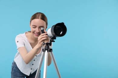 Happy astronomer looking at stars through telescope on light blue background, space for text