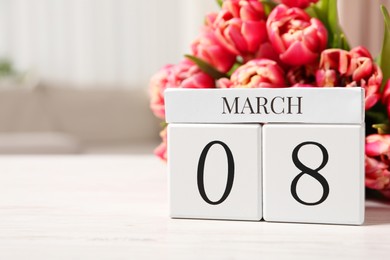 Photo of International Women's day - 8th of March. Block calendar and bouquet of beautiful tulips on white wooden table, closeup. Space for text