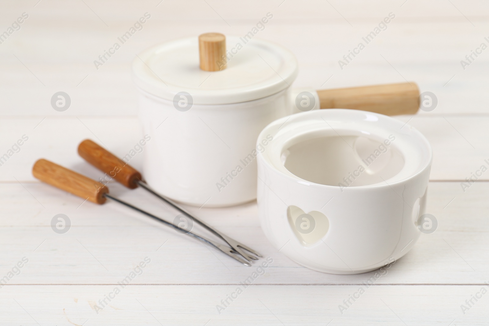 Photo of Fondue set on white wooden table, closeup