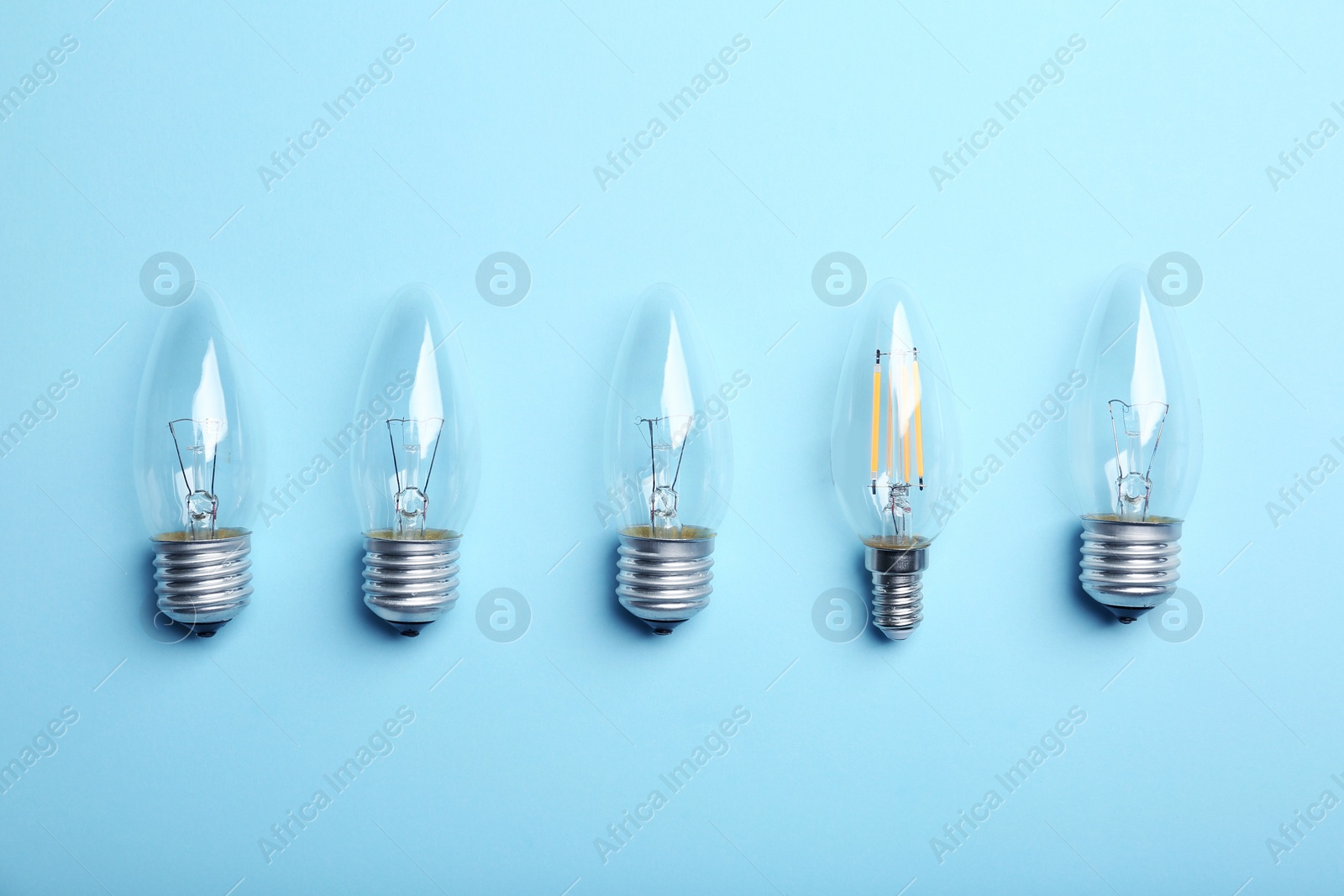 Photo of Vintage and modern lamp bulbs on light blue background, flat lay