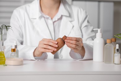 Photo of Dermatologist with bottle of cosmetic product at white table indoors, selective focus. Development and testing