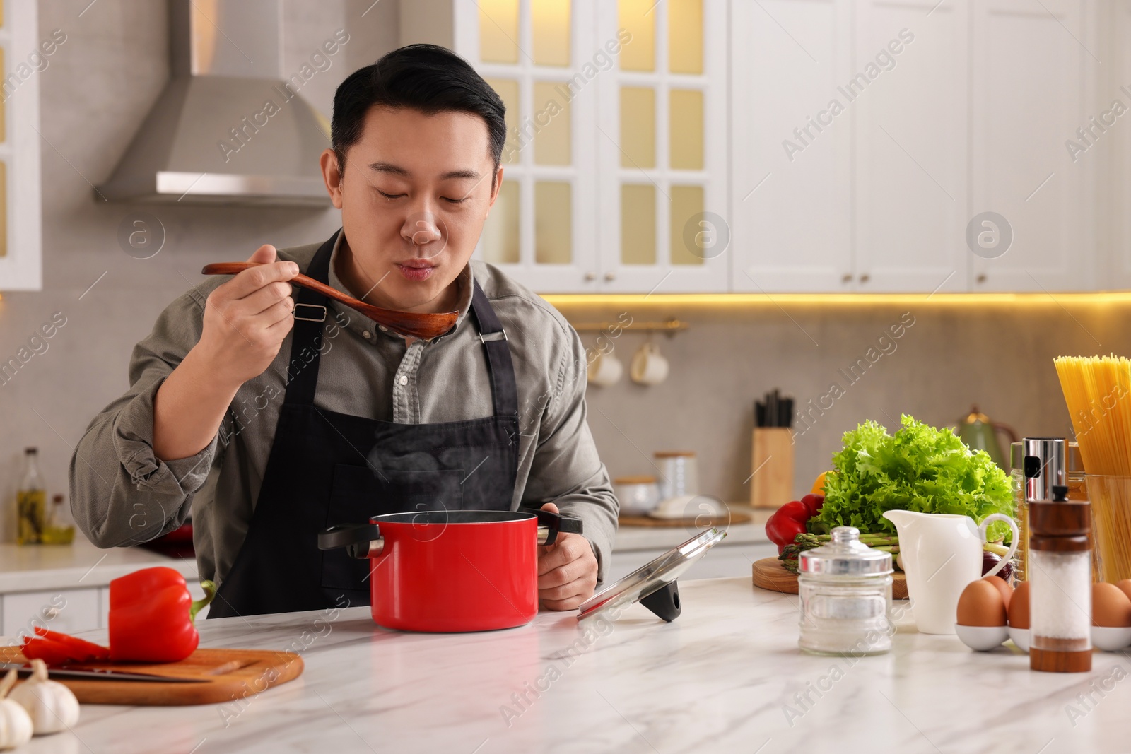 Photo of Cooking process. Man tasting dish at countertop in kitchen