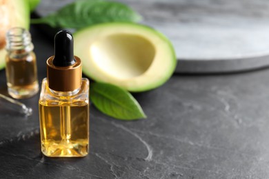 Bottle of essential oil and fresh avocado on black table, space for text