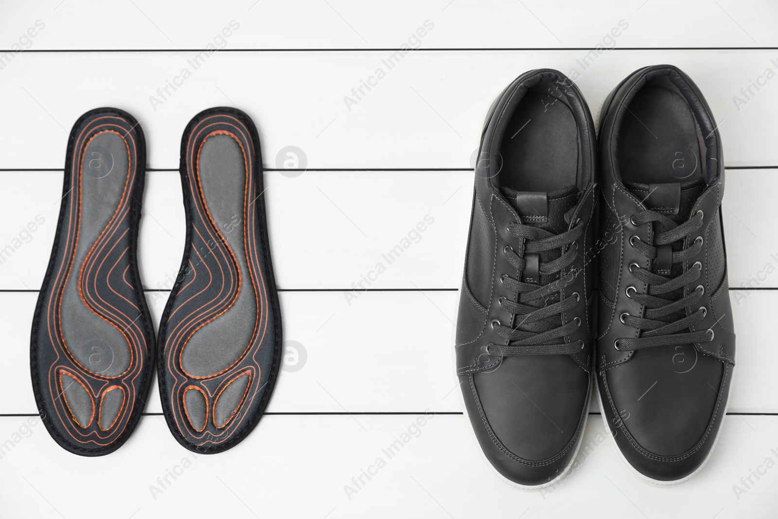 Photo of Orthopedic insoles near shoes on white wooden floor, flat lay