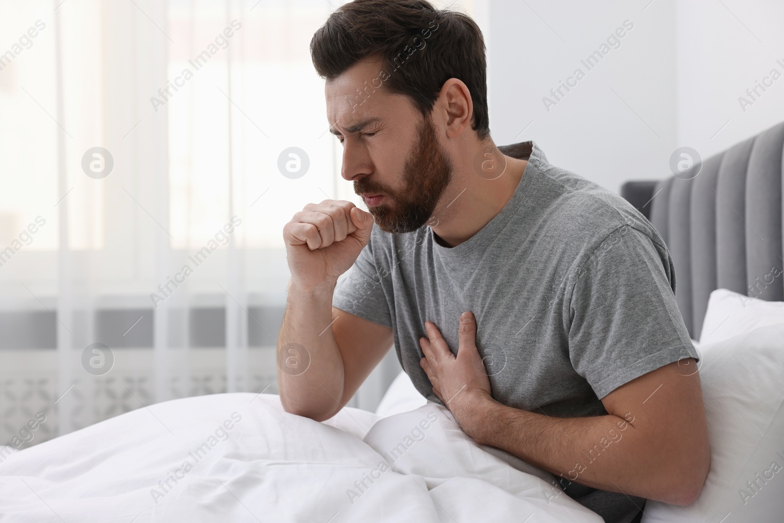 Photo of Sick man coughing on bed at home. Cold symptoms