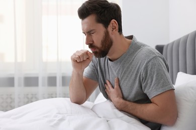 Photo of Sick man coughing on bed at home. Cold symptoms