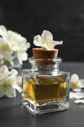 Photo of Jasmine essential oil and fresh flowers on dark grey table