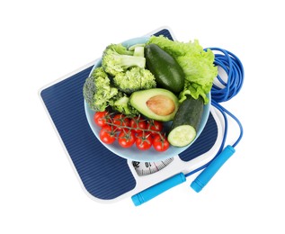 Photo of Skipping rope and bowl with different vegetables on scales isolated on white, top view. Weight loss concept