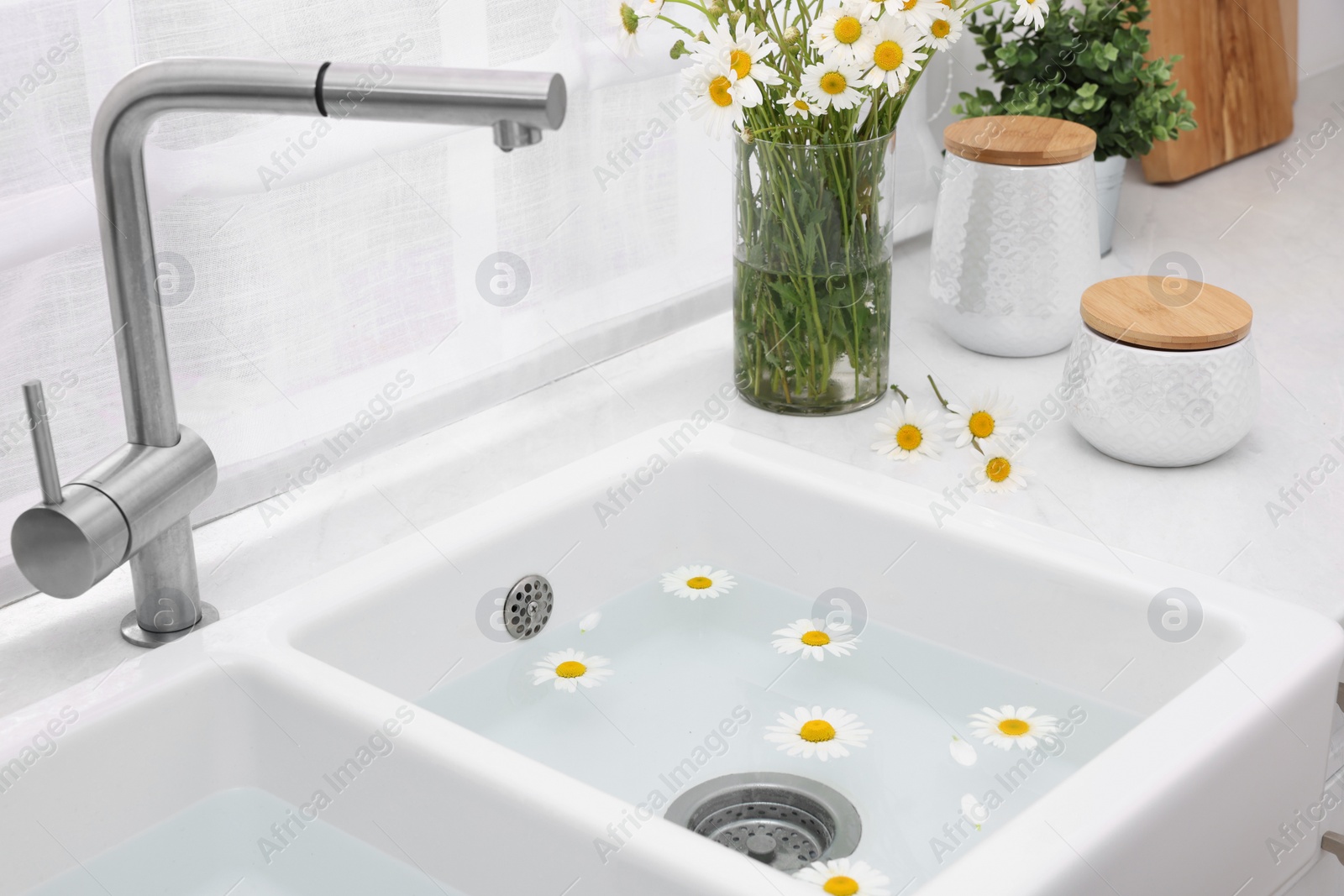 Photo of Sink with water and beautiful chamomiles indoors