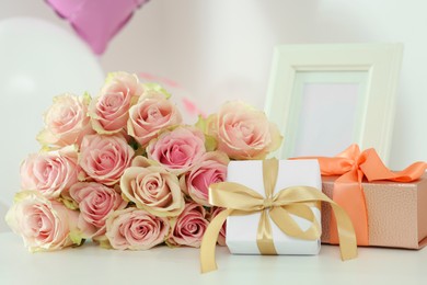 Photo of Beautiful bouquet of roses, gifts and balloons on white table. Happy birthday greetings