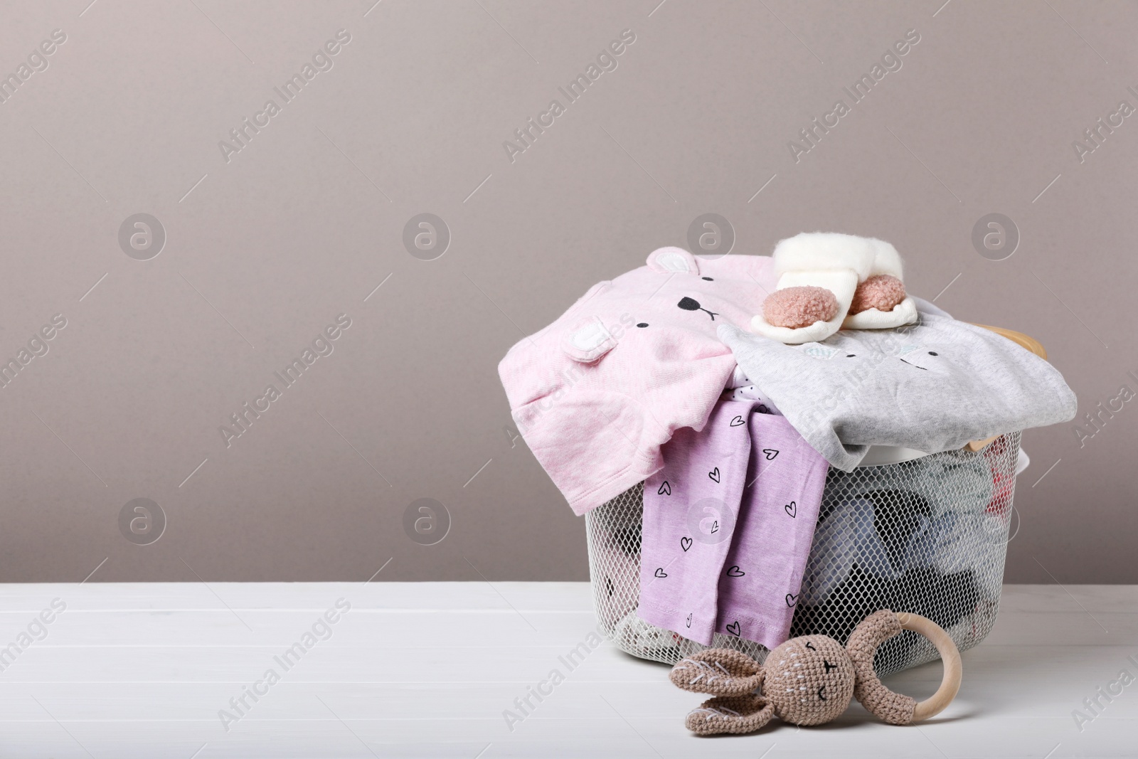 Photo of Laundry basket with baby clothes and soft toy on white wooden table, space for text
