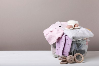 Laundry basket with baby clothes and soft toy on white wooden table, space for text