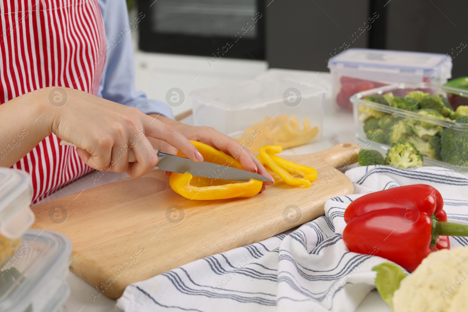 Photo of Woman cutting bell pepper near food storage containers at table in kitchen, closeup