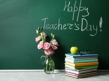 Green chalkboard with inscription HAPPY TEACHER'S DAY, vase of flowers and books on grey stone table. Space for text