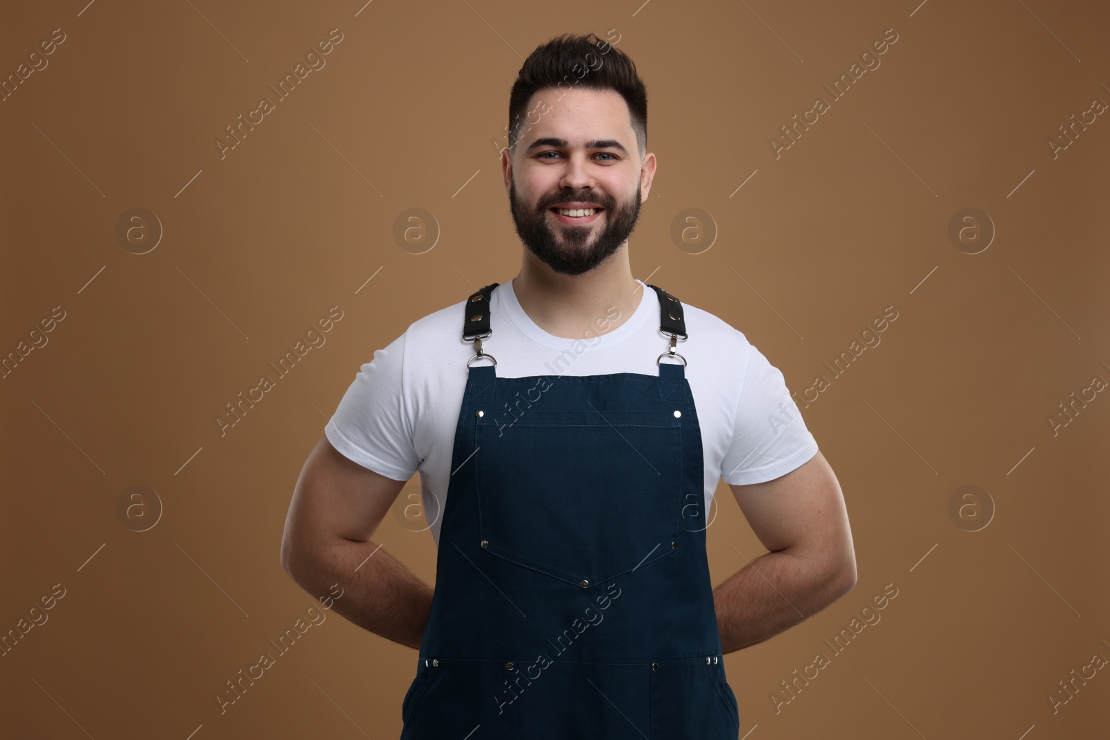 Photo of Smiling man in kitchen apron on brown background. Mockup for design