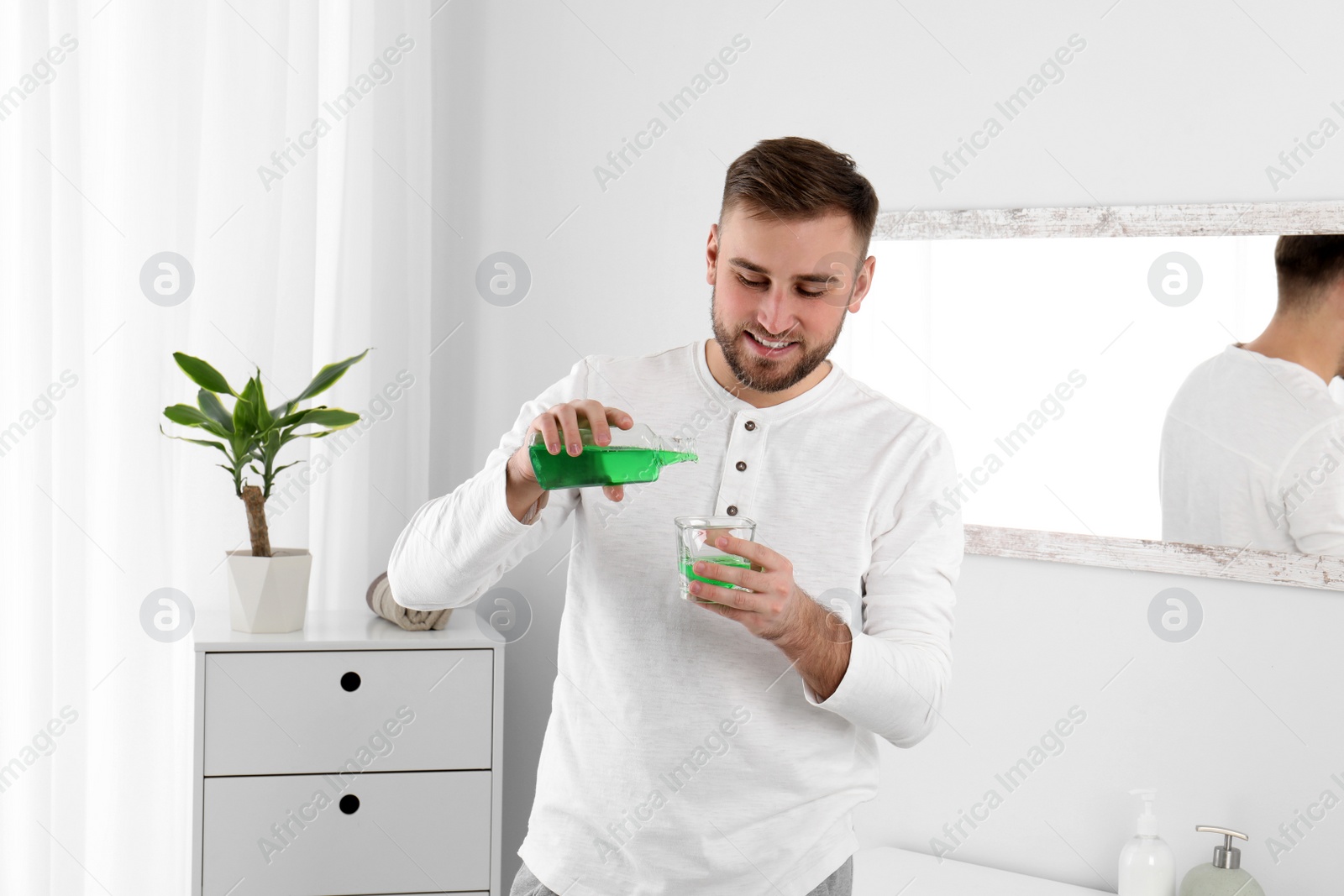 Photo of Young man with mouthwash in bathroom. Teeth and oral care