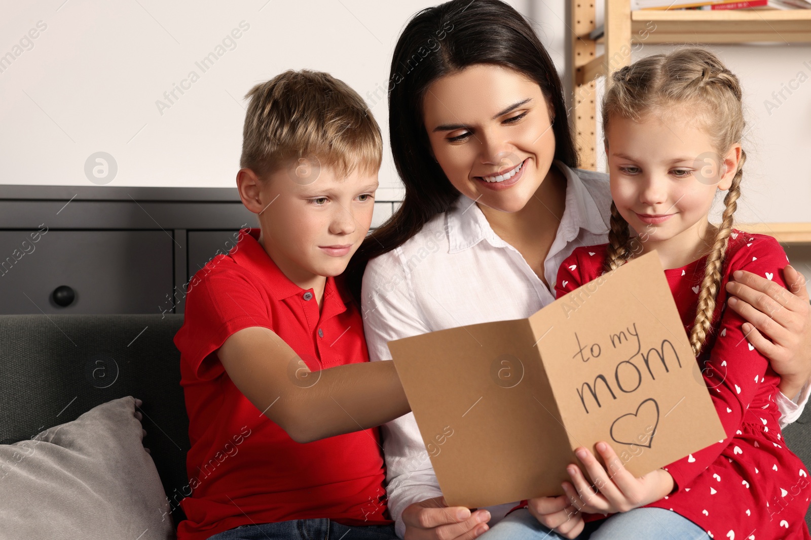 Photo of Happy woman receiving greeting card from her children at home