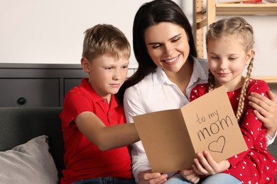 Happy woman receiving greeting card from her children at home