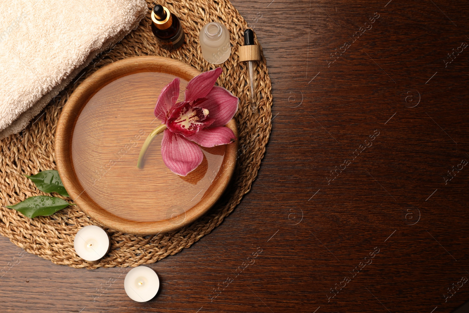 Photo of Water with beautiful flower in bowl, bottles of essential oil and candles on wooden table, flat lay with space for text. Aromatherapy treatment