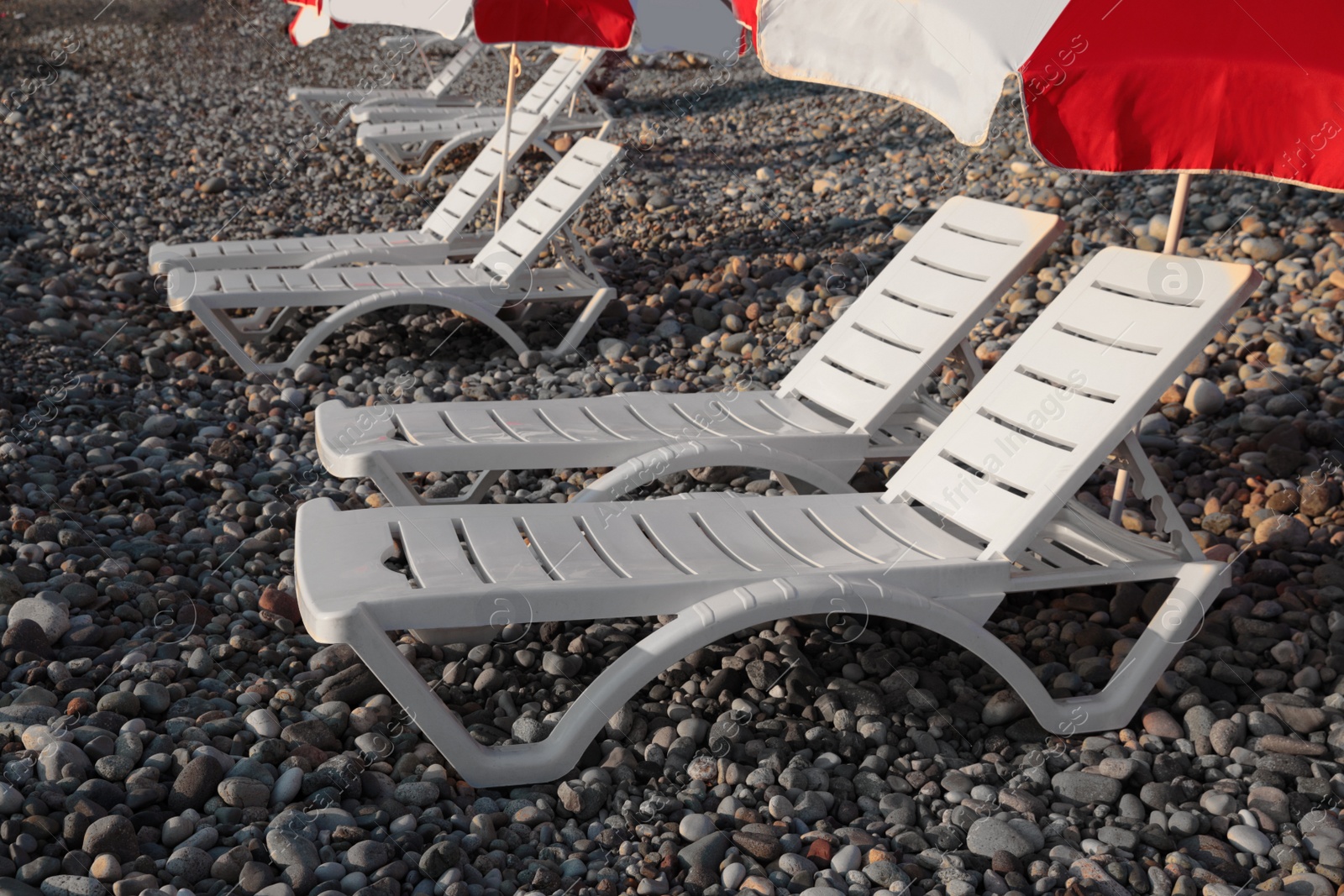 Photo of Empty sunbeds and umbrella on stone beach outdoors