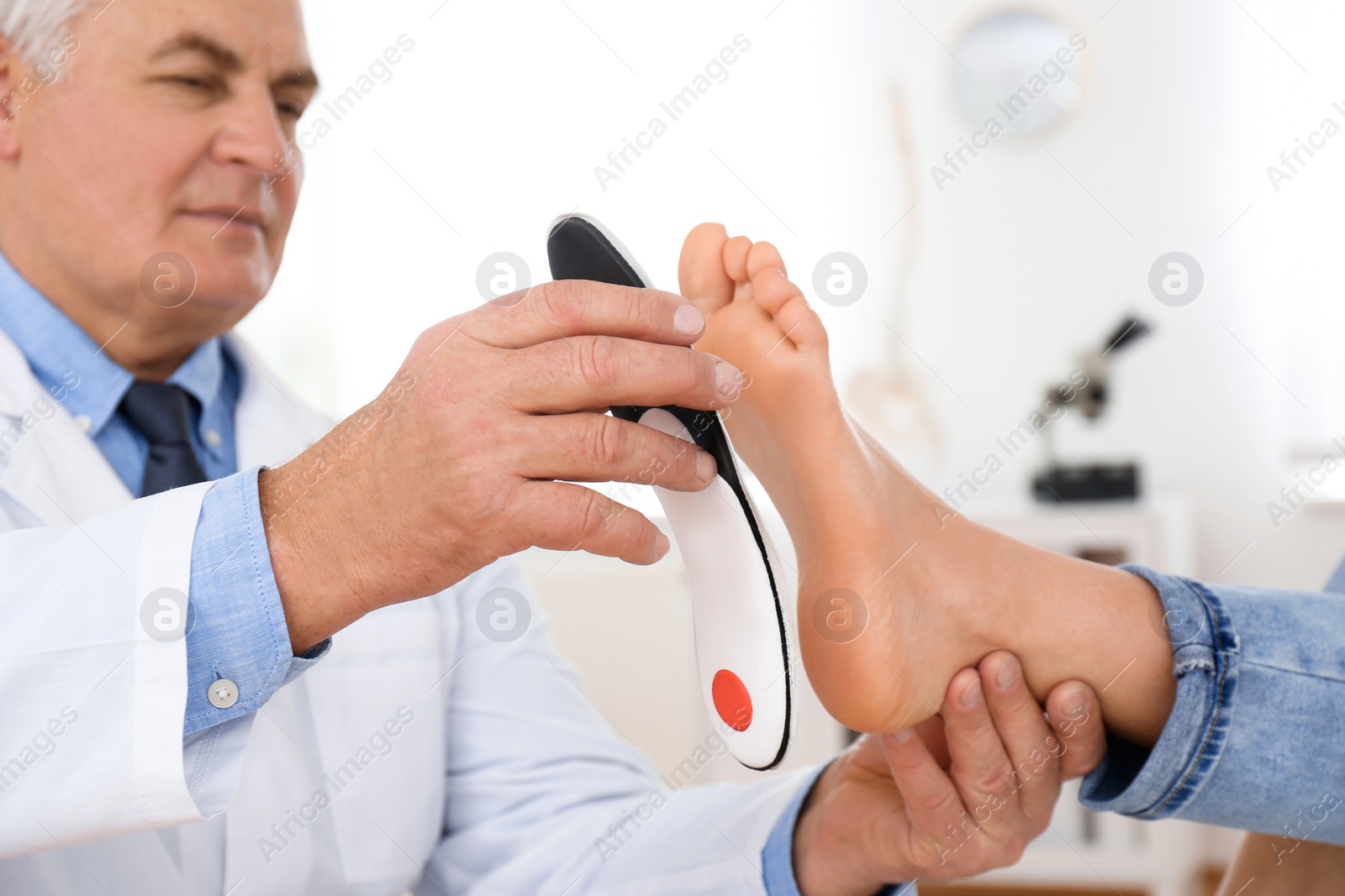 Photo of Male orthopedist fitting insole on patient's foot in clinic