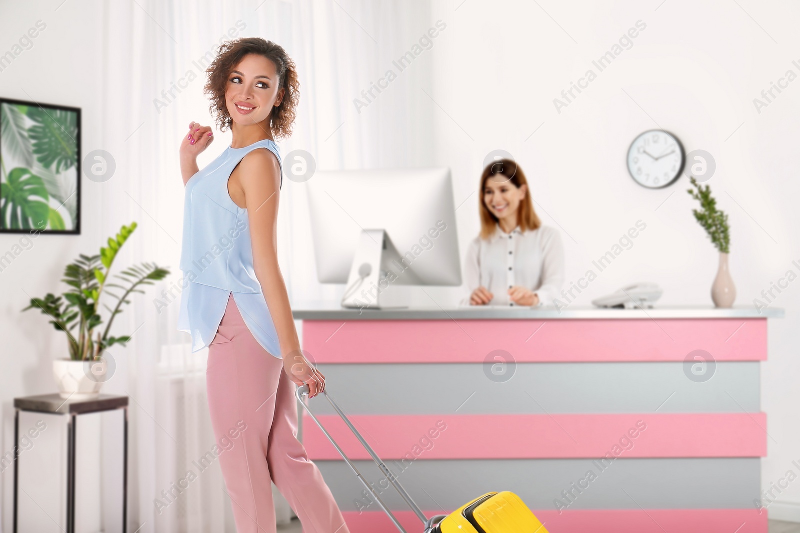 Image of Beautiful woman with suitcase near receptionist in hotel