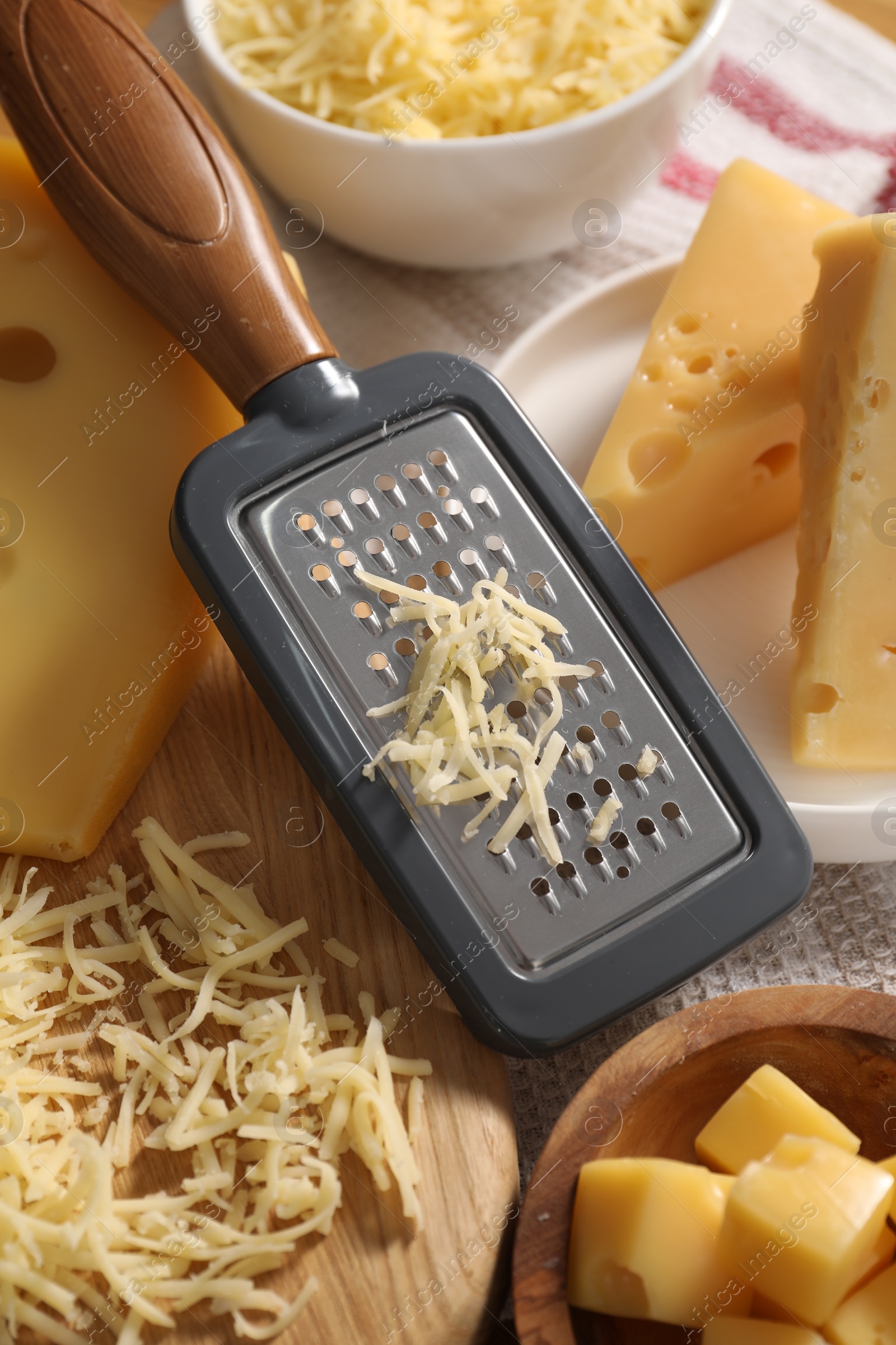 Photo of Grated, cut cheese and grater on table, closeup