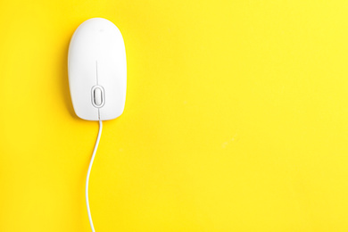 Modern wired optical mouse on yellow background, top view. Space for text