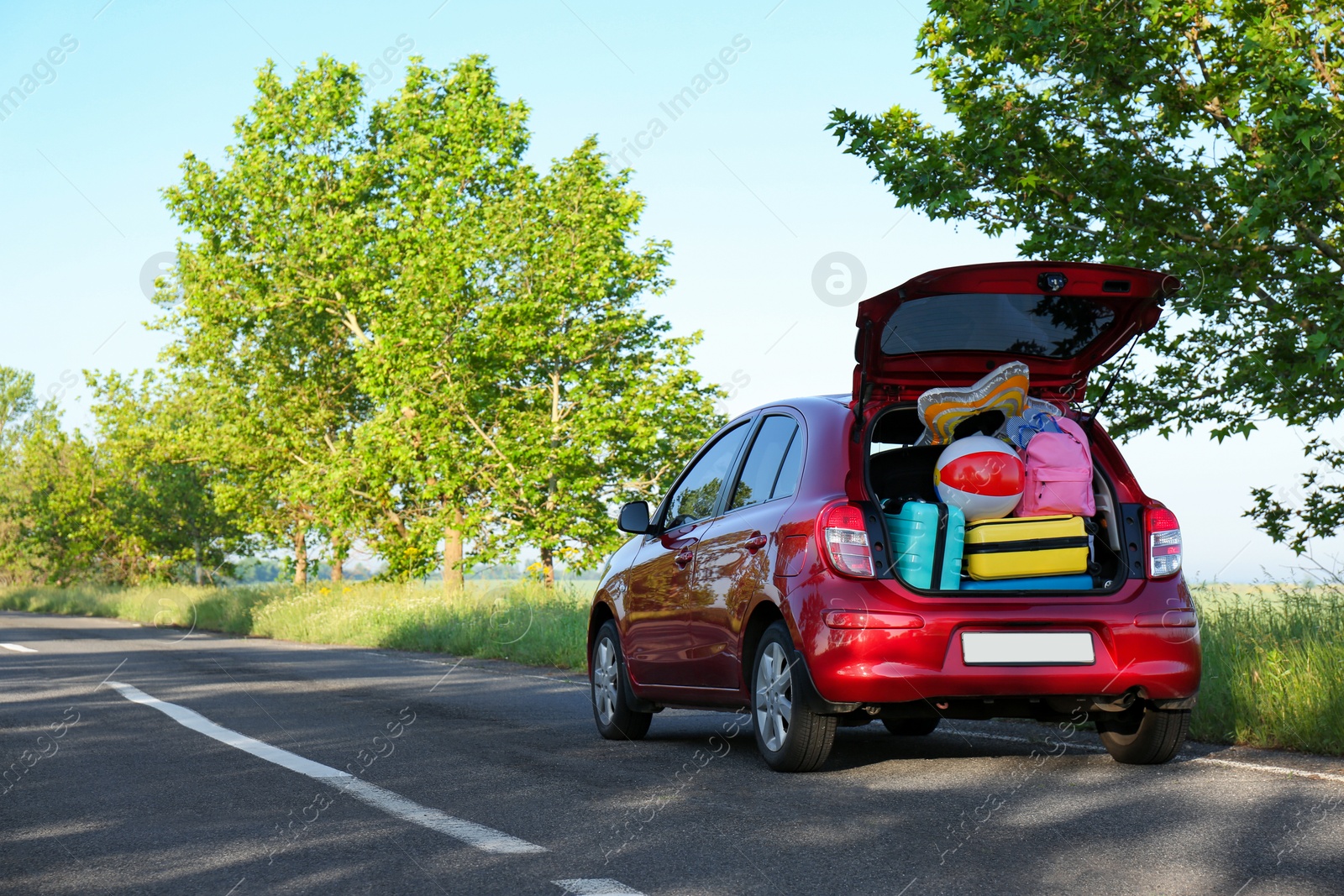 Photo of Family car with open trunk full of luggage on highway. Space for text