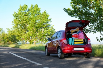 Photo of Family car with open trunk full of luggage on highway. Space for text