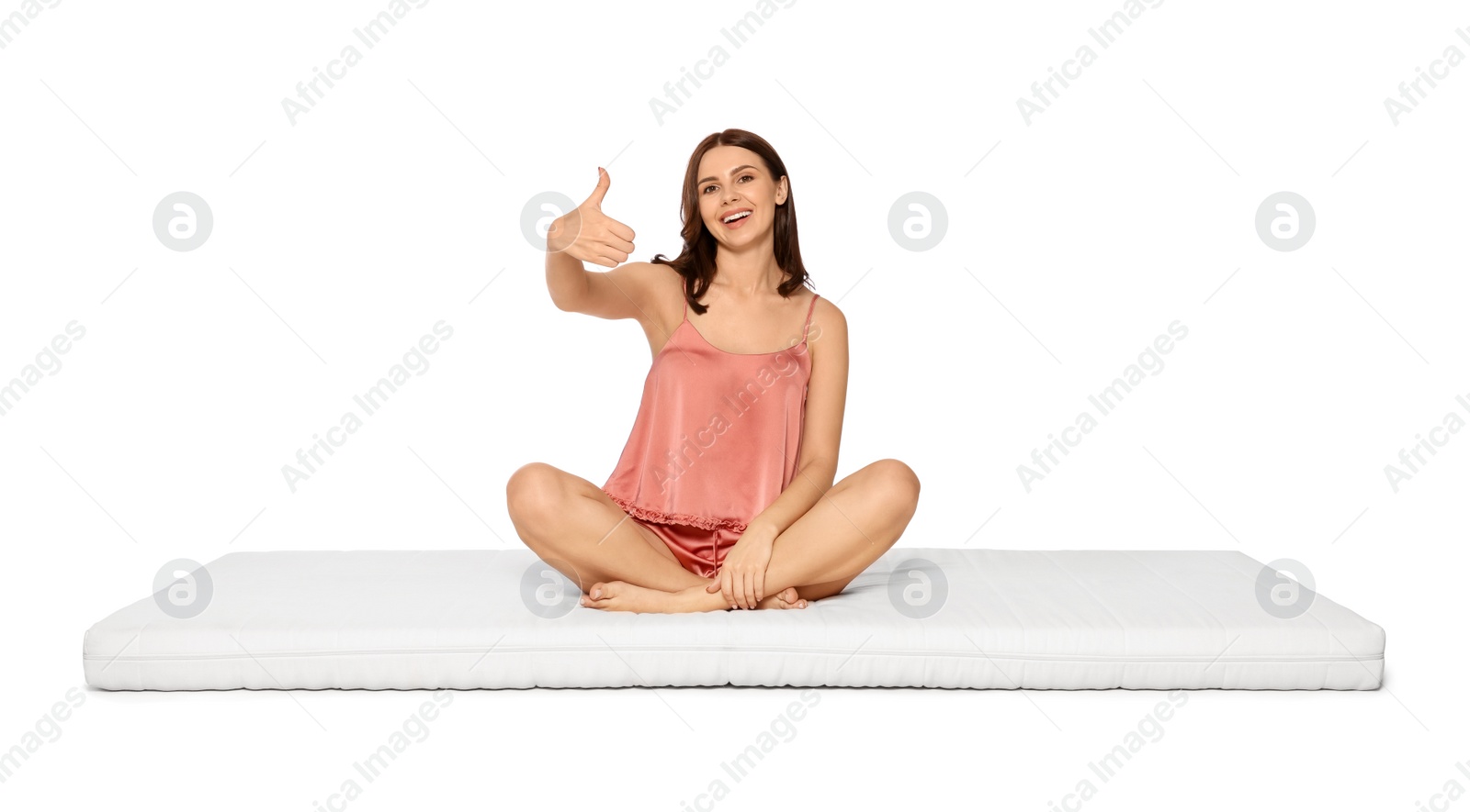 Photo of Young woman sitting on soft mattress and showing thumbs up against white background