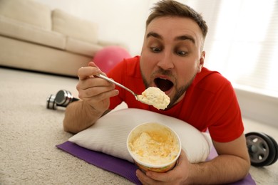 Photo of Lazy young man eating ice cream insteadtraining at home