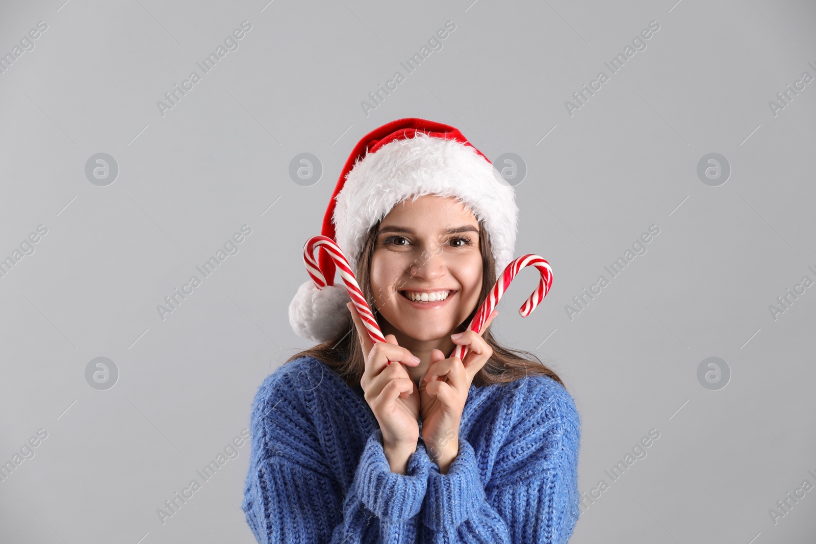 Photo of Pretty woman in Santa hat and blue sweater holding candy canes on grey background