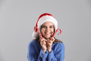 Photo of Pretty woman in Santa hat and blue sweater holding candy canes on grey background