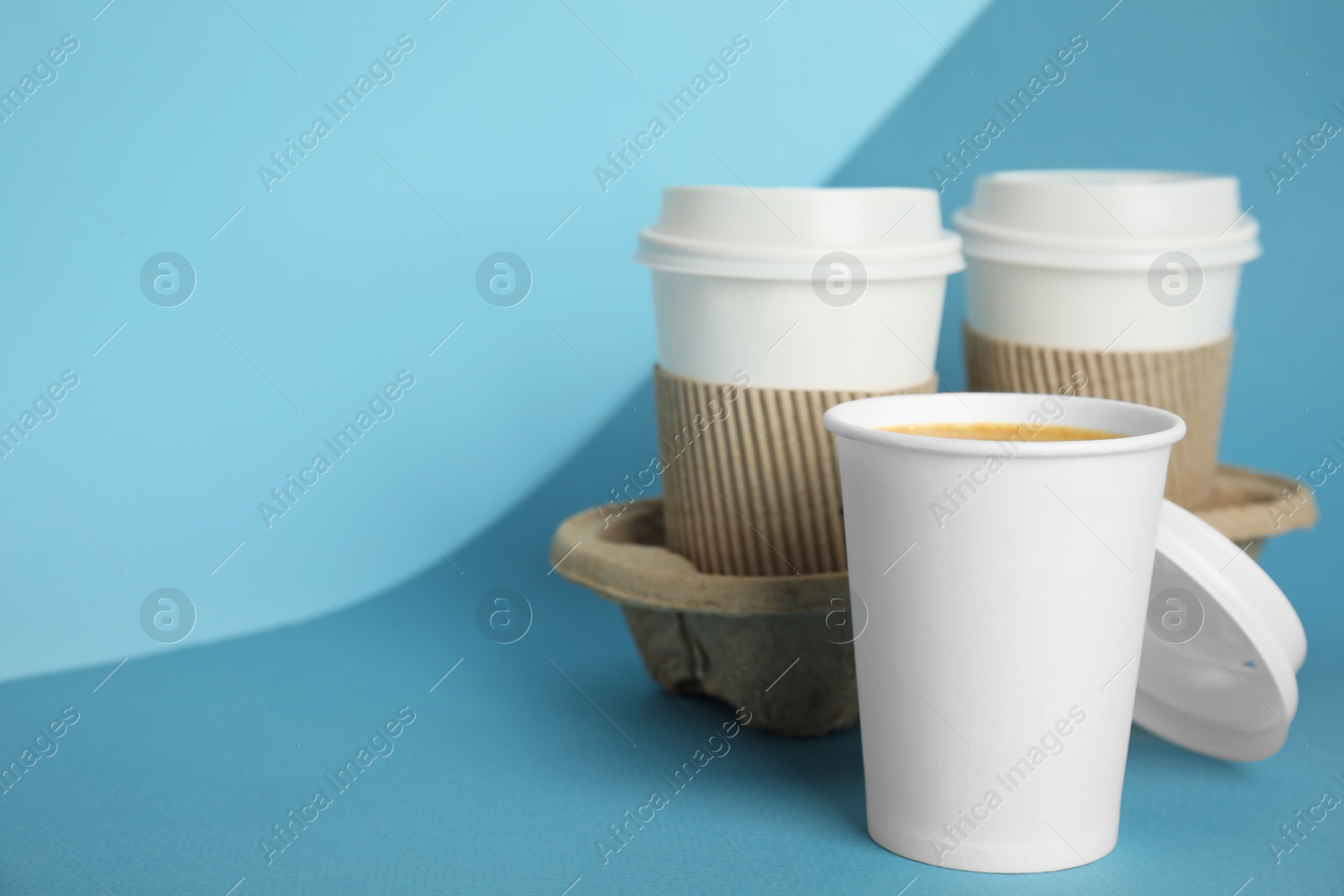 Photo of Takeaway paper coffee cups with sleeves, plastic lids and cardboard holder on blue background, space for text