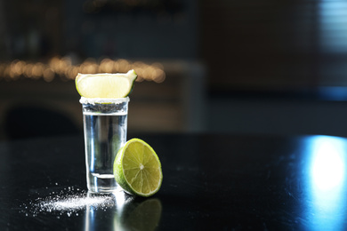 Photo of Mexican Tequila with salt and lime slices on black table at bar. Space for text