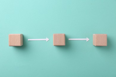 Photo of Business process organization and optimization. Scheme with wooden cubes and arrows on turquoise background, top view