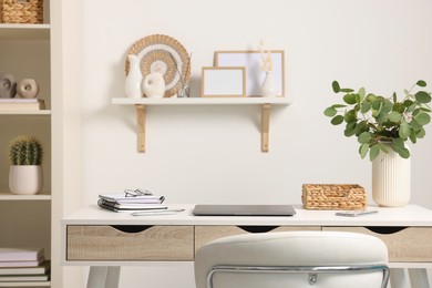 Photo of Home office. Laptop, glasses, stationery and plant on white desk indoors