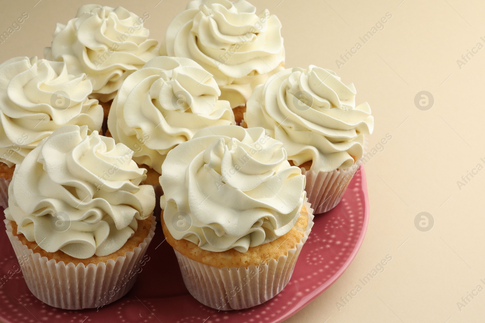 Photo of Tasty vanilla cupcakes with cream on beige table, closeup