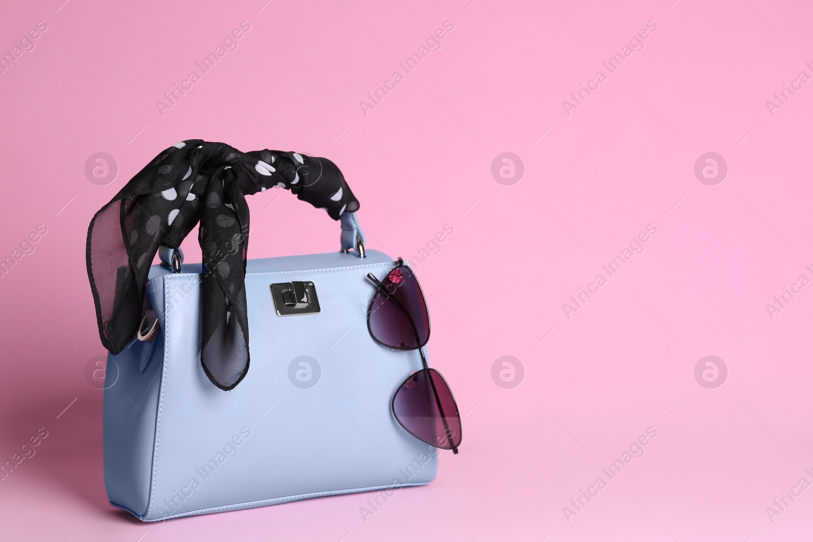 Photo of Stylish woman's bag, scarf and sunglasses on light pink background. Space for text