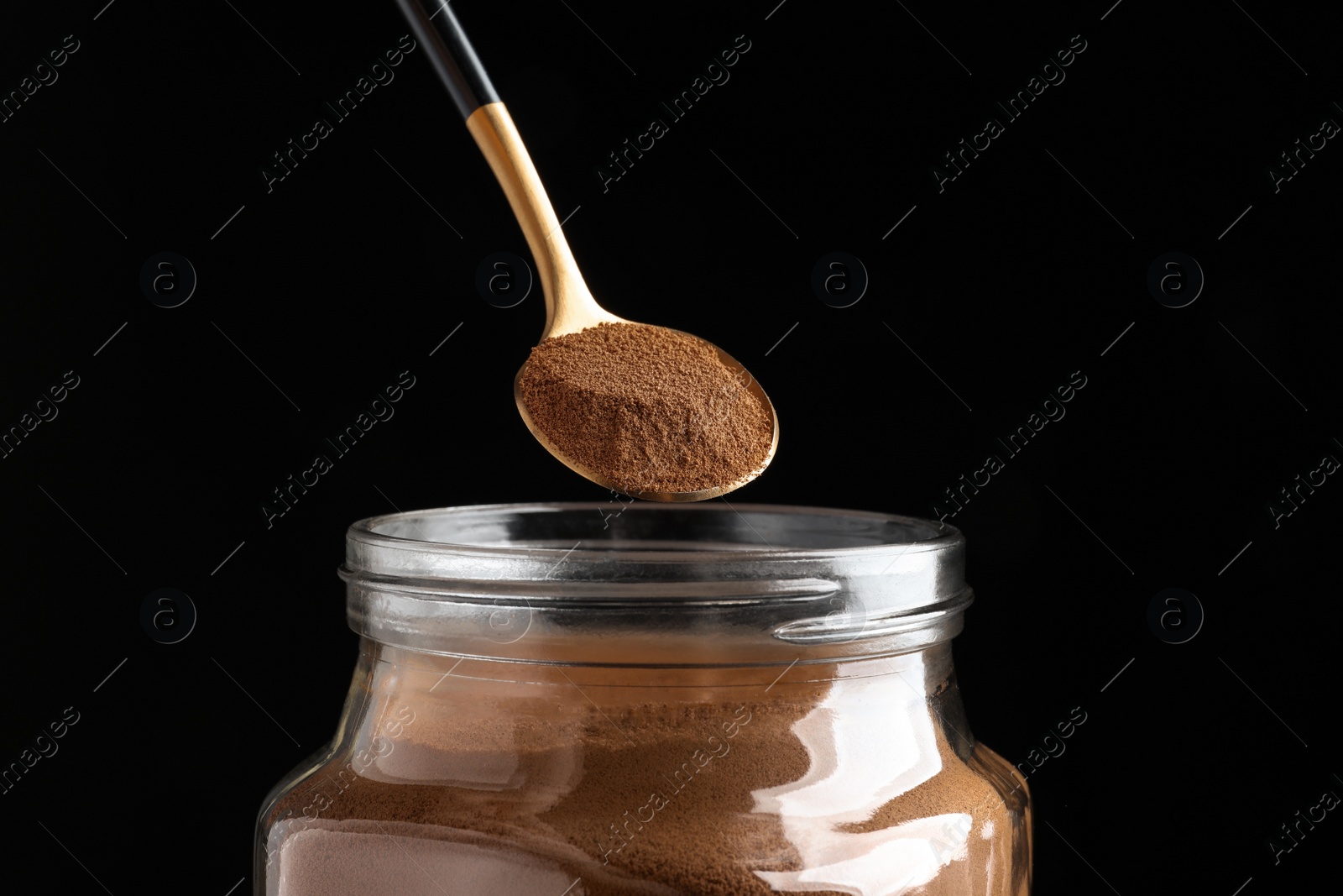 Photo of Spoon of instant coffee over jar against black background, closeup