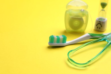 Photo of Tongue cleaner, toothbrush, dental floss and hourglass on yellow background, closeup. Space for text